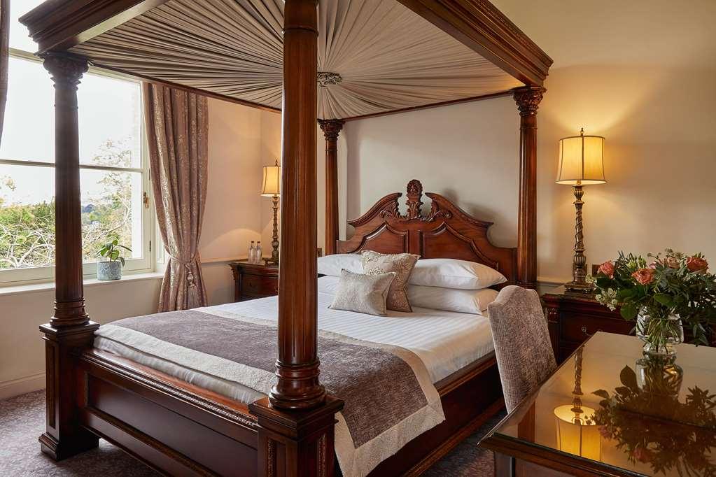 Macdonald Bath Spa Hotel Habitación foto The photo shows a beautifully designed bedroom featuring a four-poster bed made of dark wood. The bed has an elaborately carved headboard and is adorned with a light-colored bedding set. Above the bed, there is a canopy that adds an elegant touch. On