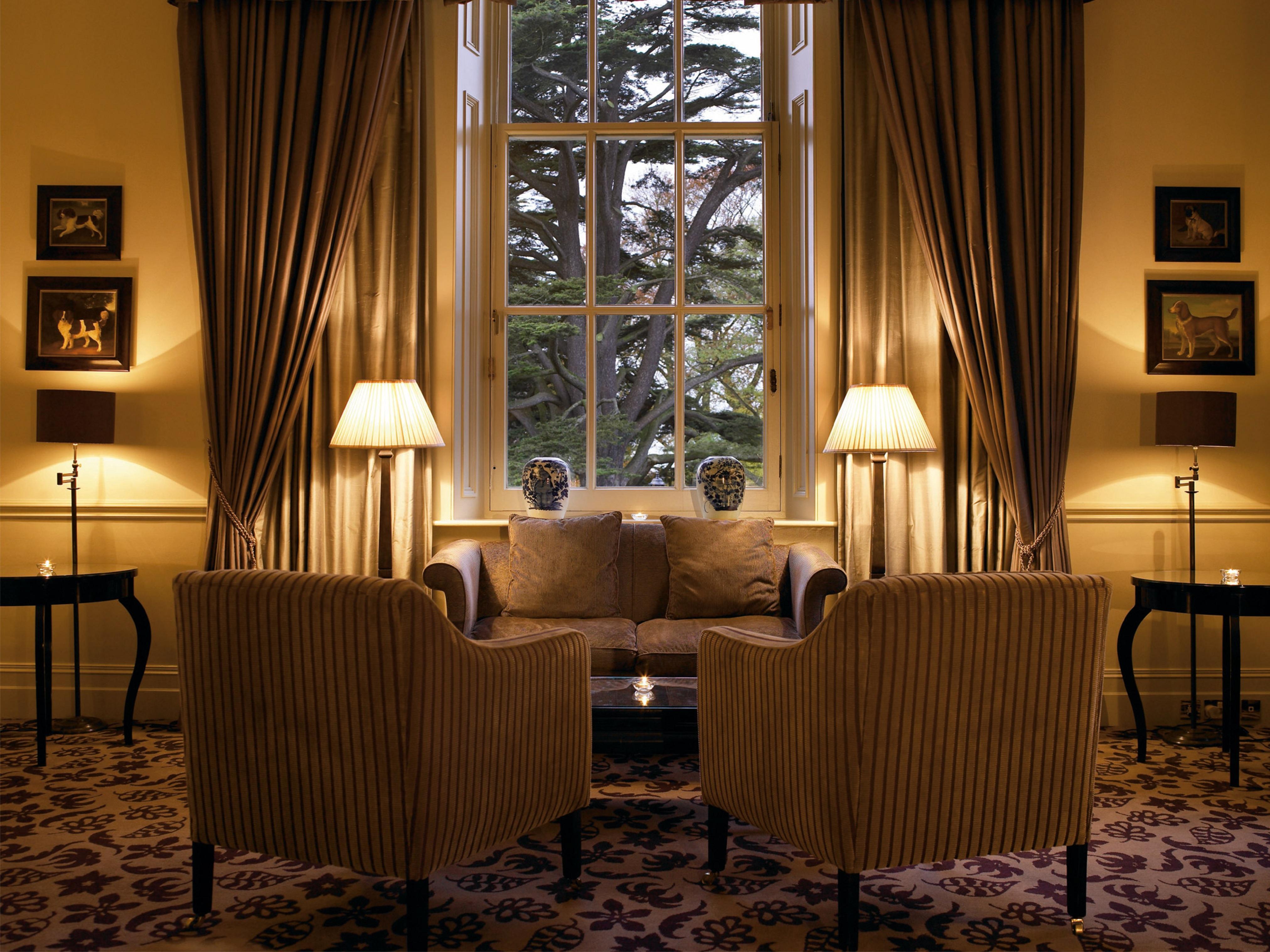 Macdonald Bath Spa Hotel Exterior foto The photo shows a cozy and elegant sitting area. There are two upholstered armchairs facing a small sofa, all arranged around a central coffee table. Soft lighting is provided by two lamps with white shades, one beside each chair. The window behind t