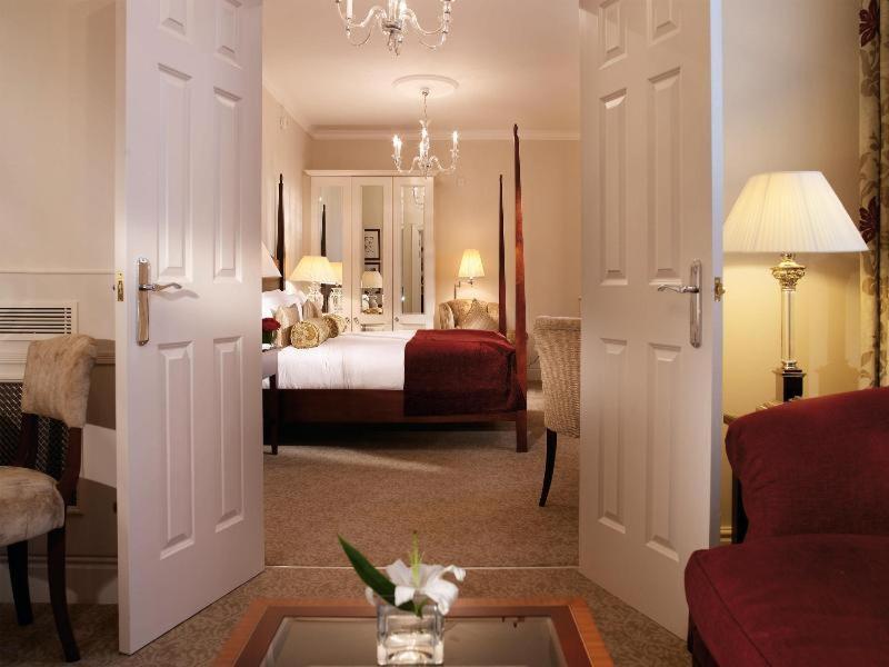 Macdonald Bath Spa Hotel Habitación foto The photo shows a hotel room that can be viewed through open double doors. Inside, there is a neatly made bed with decorative pillows, a plush area rug, and soft lighting from lamps. The room features elegant furnishings, including a chair, a coffee 