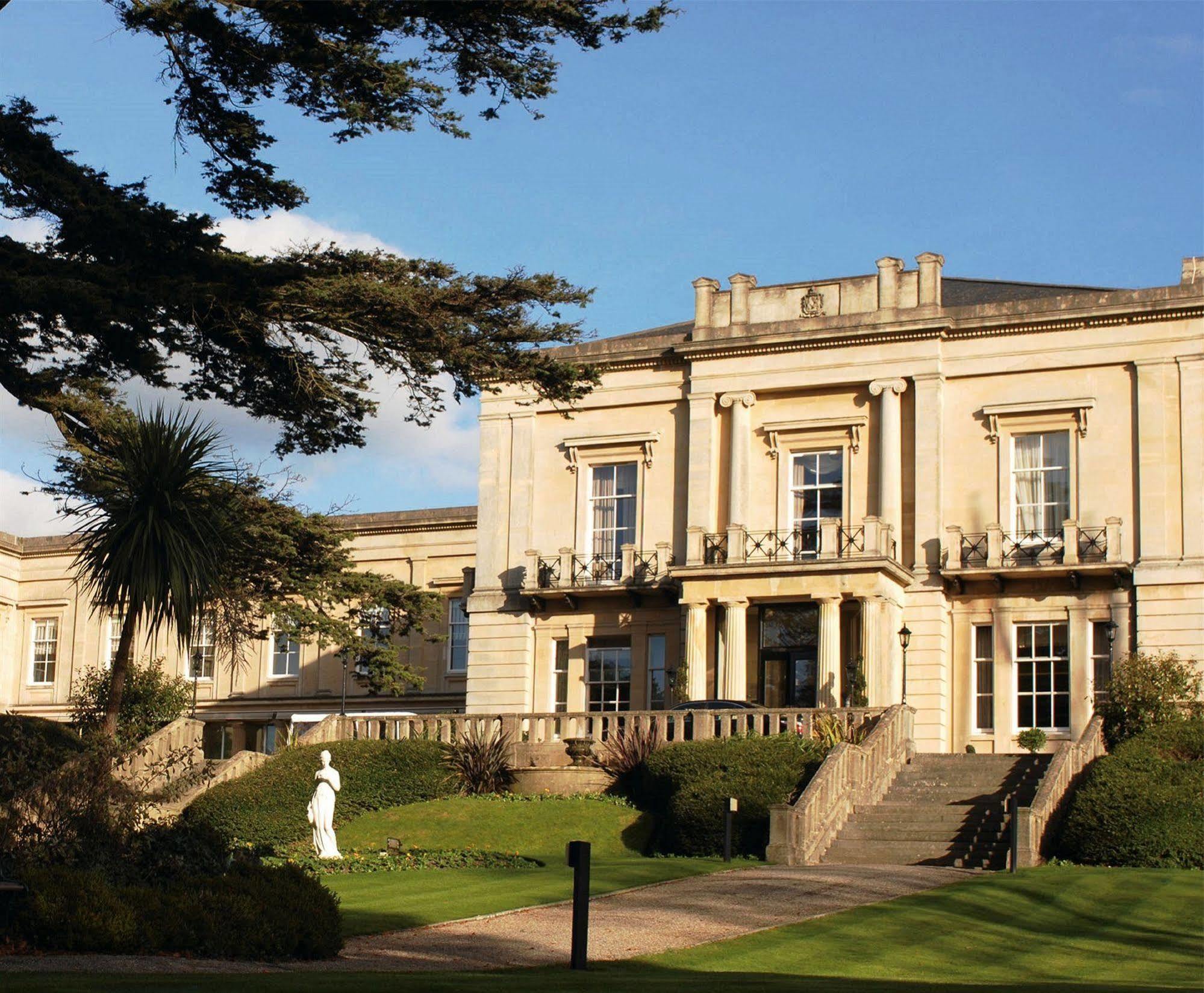 Macdonald Bath Spa Hotel Exterior foto The photo shows an elegant building with classical architecture, featuring large windows and decorative elements. The facade is light-colored, and there are several balconies. In front of the building, there is a landscaped area with greenery, includ